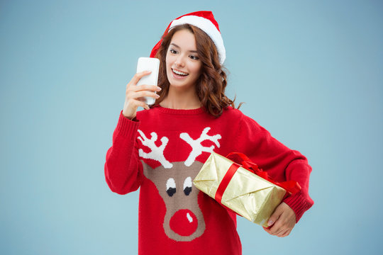 Girl dressed in santa hat with a Christmas gift and phone