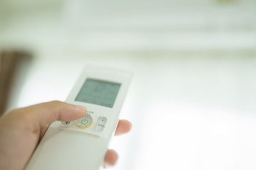 Hand of the man turning on air conditioning,Air condition and remote control,Hand with remote control directed on the conditioner.Selective focus.