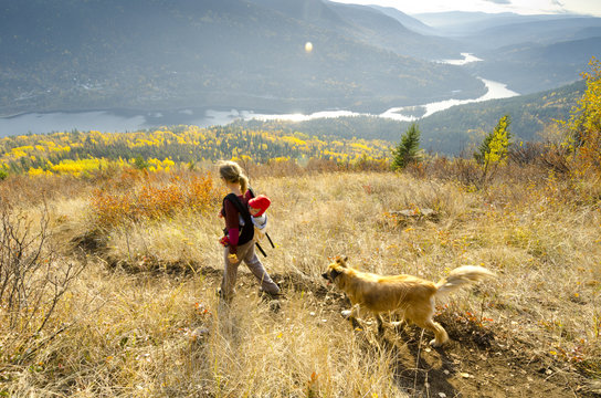 A young woman, carrying her child and hiking with a dog above the Kootenay River up Nelson's Pulpit Rock Trail, Nelson, British Columbia