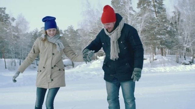 Young woman and her boyfriend skating together clumsily on outdoors ice rink in park