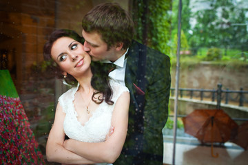 Look from the outside at tender groom kissing bride while huggin