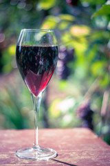Glass with red wine on the wooden table. Shallow depth of field. Toned image.