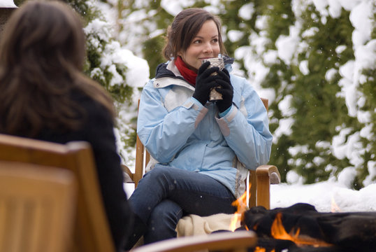 A teenage girl enjoys a hot drink in the winter snow by an outdoor fire.