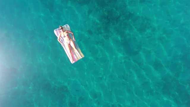 Woman relaxing and sunbathing on the inflatable beach mattress on the sea aerial view