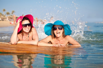 Obraz na płótnie Canvas Two beautiful happy girl in colored hat splash in the sea water on a hot day at the spa