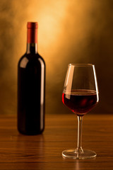 Red wine bottle with glass on gold background

