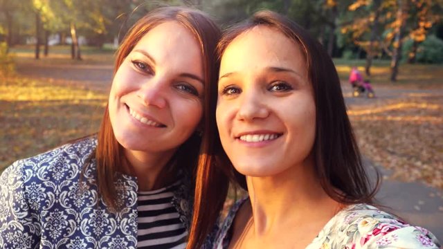 Two nice-looking cheerful girls making selfie photo in autumn park. 3840x2160