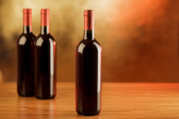Fototapeta na wymiar Three bottles of red wine on wooden table and golden background
