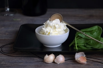 Cottage cheese, mascarpone, ricotta, sour cream, yogurt with vintage spoon, garlic and herbs in porcelain bowl against black background. Special light, selective focus.
