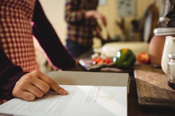 Mid-section of woman reading a recipe book in kitchen