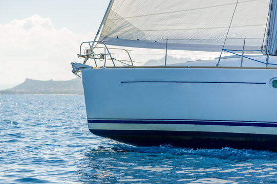 Close view against the sun at sailboat bow with hoisted headsail.