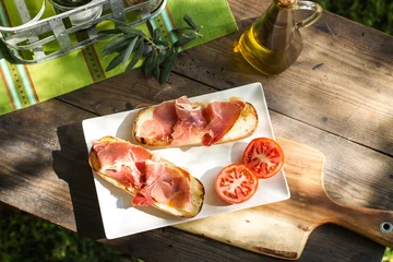 Selbstklebende Fototapete Vorspeise Tostadas con jamón serrano y aceite de oliva sobre una mesa de madera rústica al aire libre. Vista superior