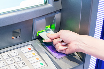 Close-up of woman's hand inserting debit card into an ATM machine. Horizontal shot.
