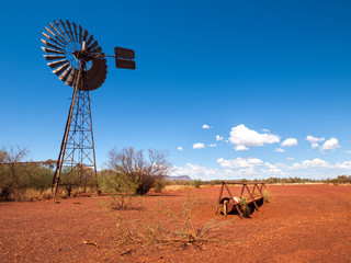 an old rusty wind turbine and cattle feeder,  in the harsh arid red landscape of the australian...