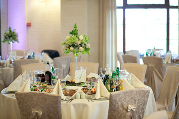 High crystal vase with green bouquet stands on the creamy dinner