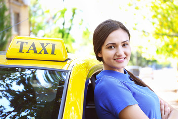 Beautiful female taxi driver standing near car