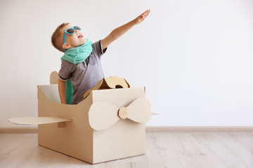 Little boy playing with cardboard airplane on white wall background - Powered by Adobe
