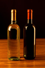 Fototapeta na wymiar White and red wine bottles on wooden table and black background