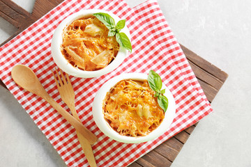 Portions of pasta Al Forno in ceramic bowls and red napkin on wooden board