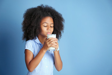 Cute curly African-American girl drinking milk on a blue background