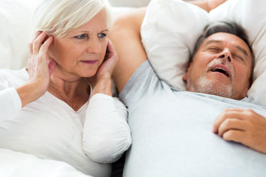 Senior man snoring and woman covering ears
