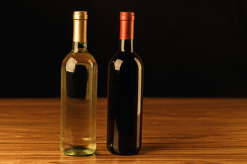 Fototapeta na wymiar Red and white wine bottles on wooden table and black background