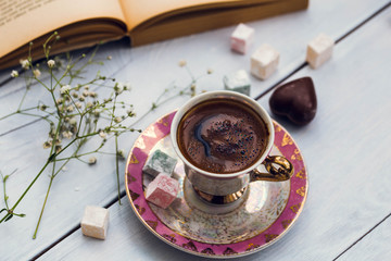 Cup of Turkish coffee with Turkish delights and heart shaped chocolate next to the old book, wooden...