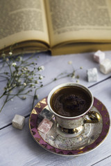 Cup of Turkish coffee with Turkish delights next to the old book, wooden background