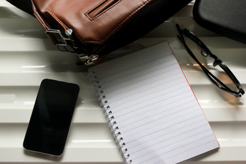 Notebook, leather bag, glasses and smart phone on desk