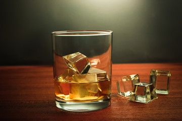 Glass of whiskey with ice on wooden background