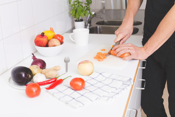 Close up on man hands cutting fresh vegetable on light interior kitchen