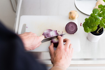 hands holding sharp knife and chopping fresh vegetables on kitchen with light surfaces