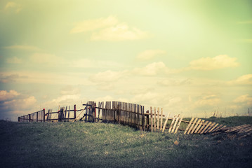 Sunny day in countryside. Summer landscape with old broken fence at pasture  under blue cloudy sky....