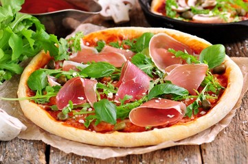 Homemade pizza with tomato sauce, mozzarella cheese, organic arugula, Parma ham, capers and parmesan cheese.