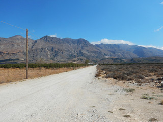 Fototapeta premium A dirty road in a flat landscape with mountains in background