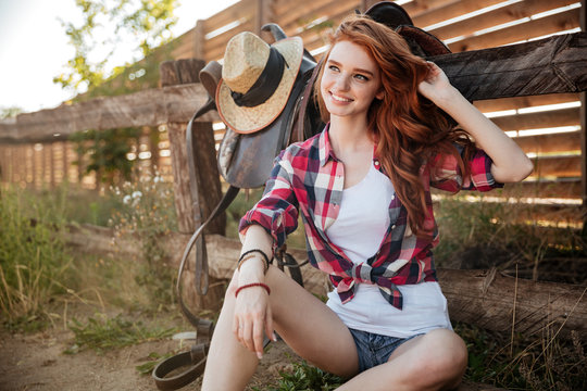 Happy smiling young cowgirl resting at the ranch fence