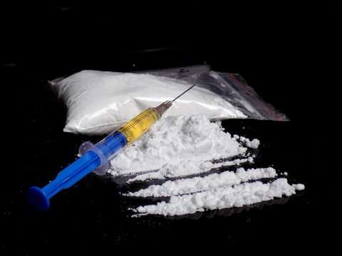 Injection syringe on cocaine drug powder pile and lines  and cocaine bag on black background