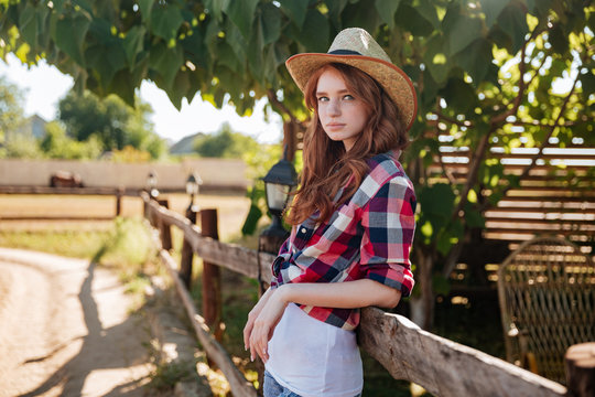 Portrait of pretty redhead cowgirl leaning on the ranch fence