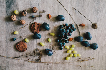 lying on wooden background grapes, plums, dry grass,seeds, thist