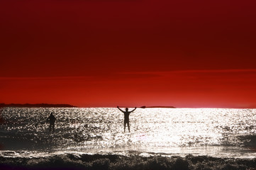 silhouette of man swim on the board in the ocean his arms raised up in which the paddle against the...