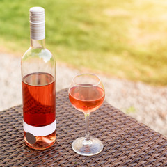 One glass and bottle of red or rose wine in autumn vineyard on wooden wicker table. Harvest time, picnic, fest theme.