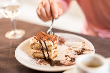 Young woman eating homemade traditional dessert tiramisu with coffee and glass of wine