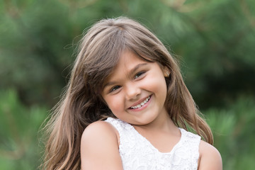 Portrait of smiling tanned brunette little girl outdoors. Little girl is looking at the camera