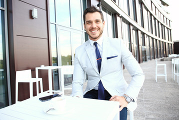 Fototapeta premium Portrait of handsome successful man drink coffee, business man having breakfast sitting on beautiful terrace