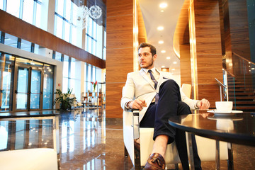 happy young businessman sitting on sofa in hotel lobby