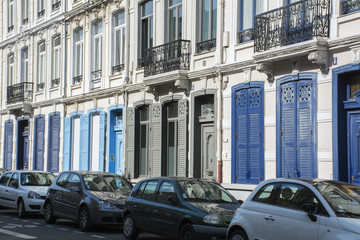 Fototapeta na wymiar Long french building with blue shutters and row of cars near it