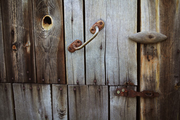 Old rusty lock hanging on the gray wooden door.