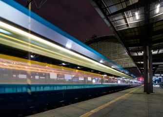 Fototapeta premium Train speeding through Prague railway station during busy night time with extended motion. Beautiful historical railway station in capital city of Czech republic.