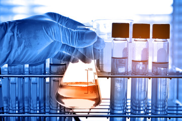 Flask in scientist hand with laboratory glassware background  