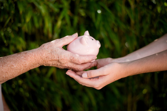 Close Up Of Elderly Woman Hand Giving Piggy Bank Money Legacy To Young Person